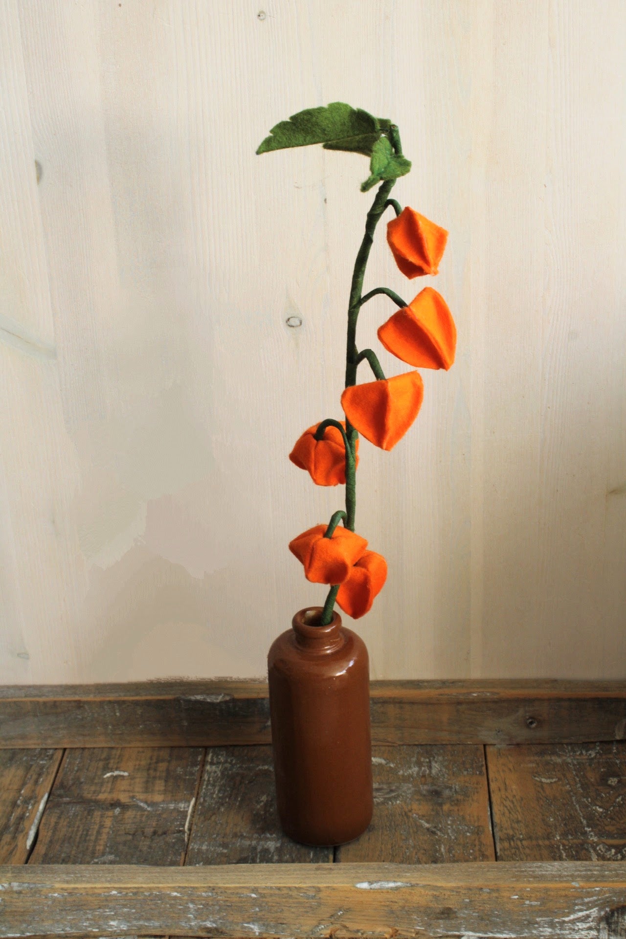 oranje lampionplantje handgemaakt van vilt in een bruin vaasje op een rustieke ondergrond 
