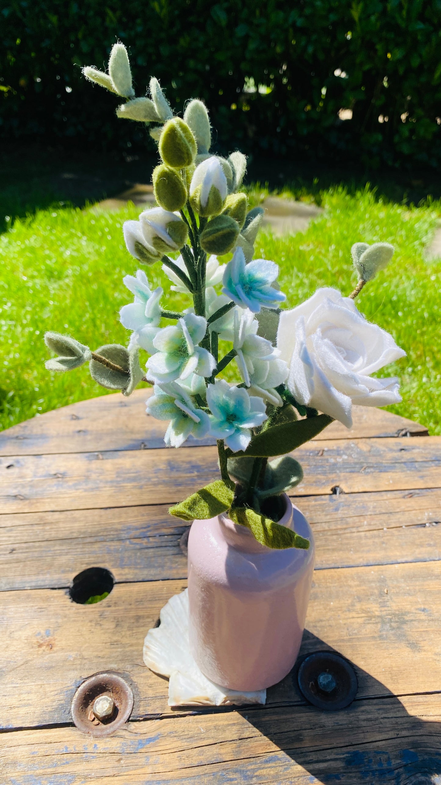 Handgemaakt Boeket viltbloemen met wtte violier, witte roos en tak eucalyptus in een roze vaas op een houten tafel en gras op de achtergrond