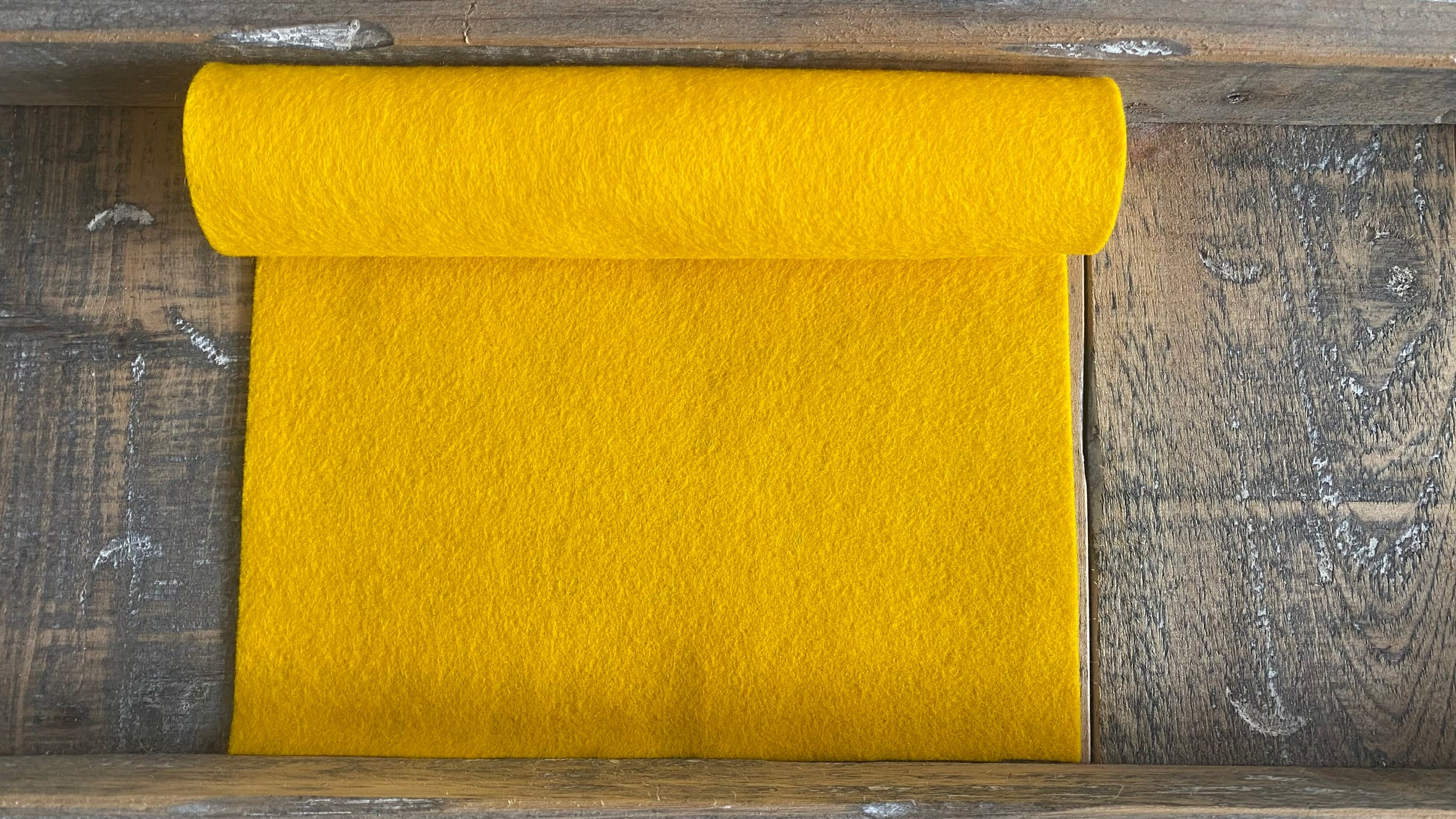 Rolletje wolvilt in de kleur geel nummer 16 op een houten ondergrond 