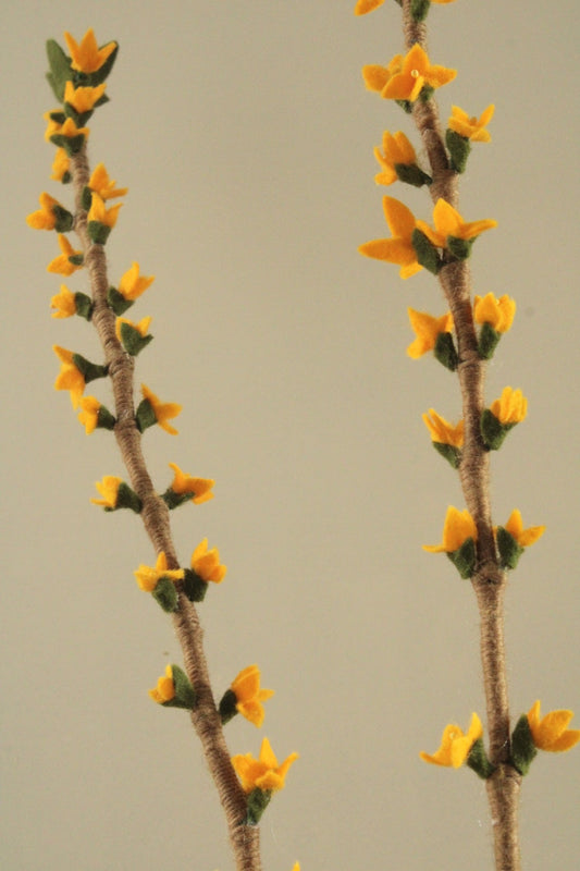 Echte tak met daarop kleine gele handgemaakte bloemetjes van wolvilt, forsythia