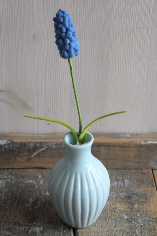 Vilten blauw druifje handgemaakt in een blauw vaasje als lente decoratie op een rustieke houten ondergrond 